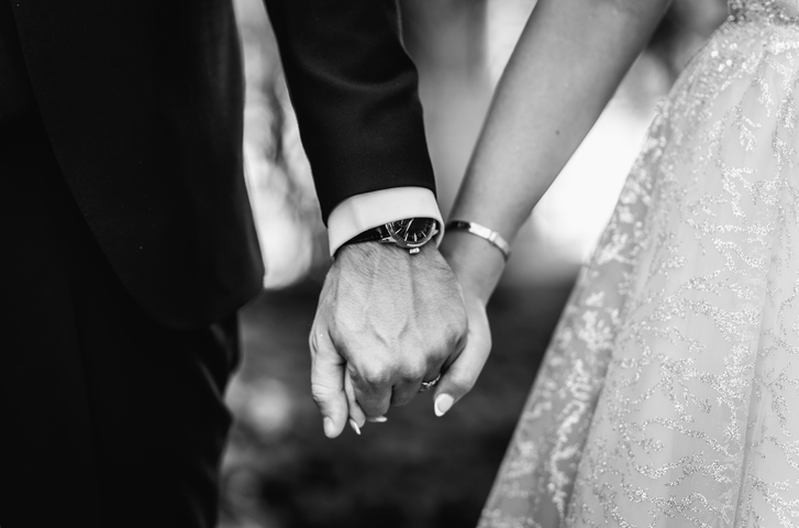 Black and white picture of bride and goorm holding hands . Focus on their wrists with a watch and bracelet